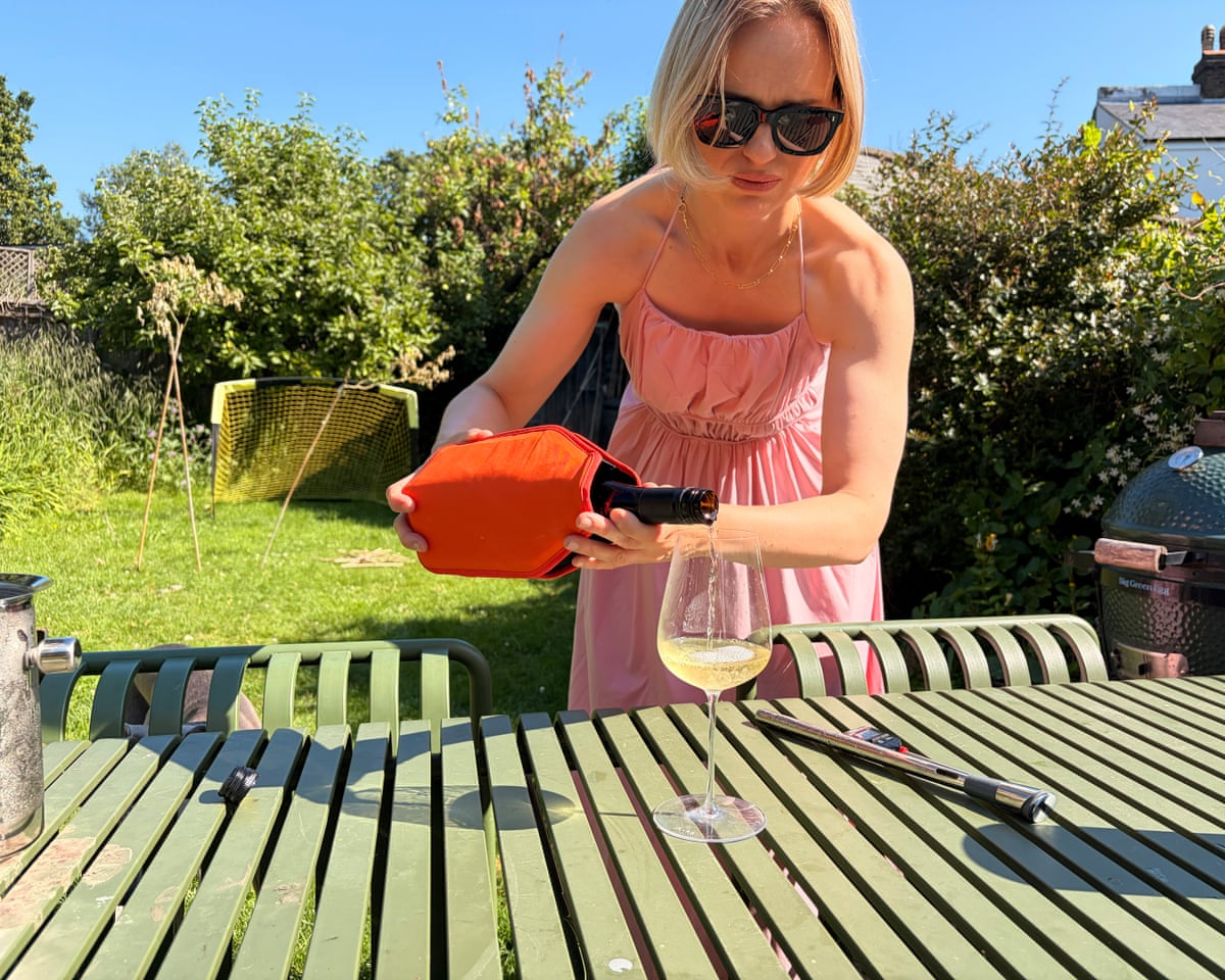 The writer pouring a glass of wine from a bottle in a Le Creuset wine cooler in a garden.