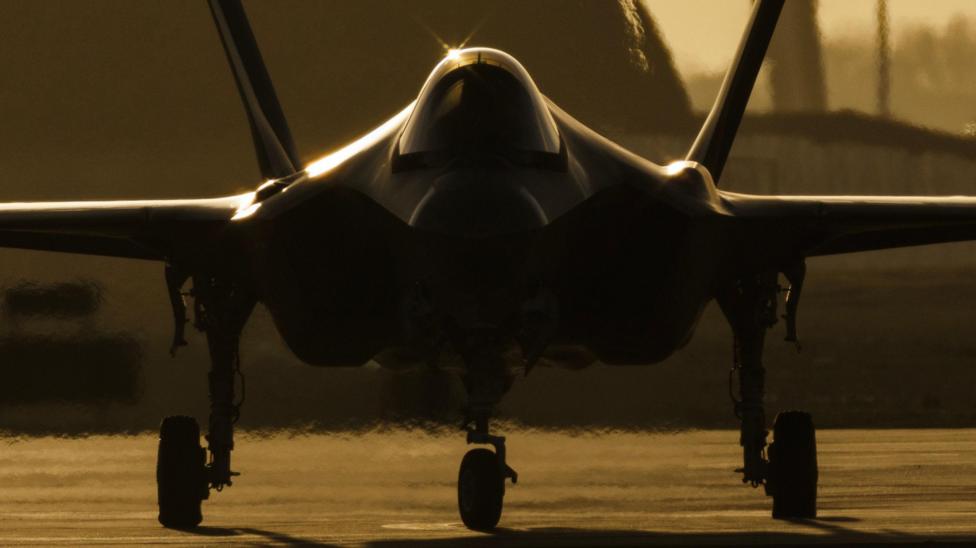The silhouette of an F-35 plane preparing to take off at sunset. The photo is taken head on.