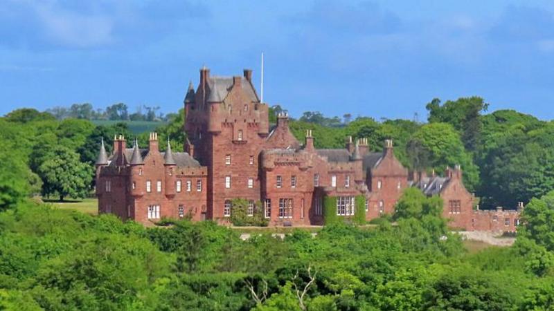 A red stone castle set among plentiful green trees