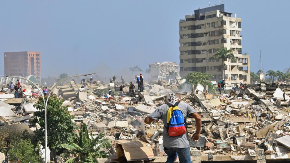 A man with a Venezuelan flag-themed backpack walks amid rubble of collapsed buildings after earthquakes hit the country.