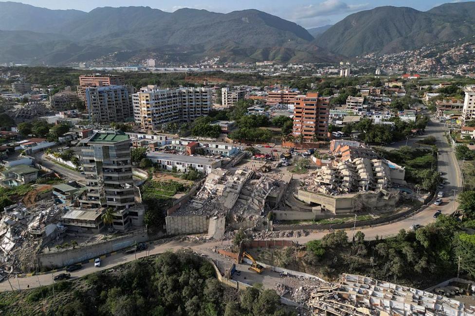 This aerial view shows collapsed buildings in Catia La Mar, La Guaira state, Venezuela, shows multiple collapsed buildings and rubble sitting in a valley with a backdrop of green mountains 