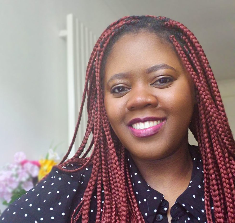 Chy, a 33-year-old woman, smiles in a close up photo. She had red braids and is wearing lipstick and smiling.