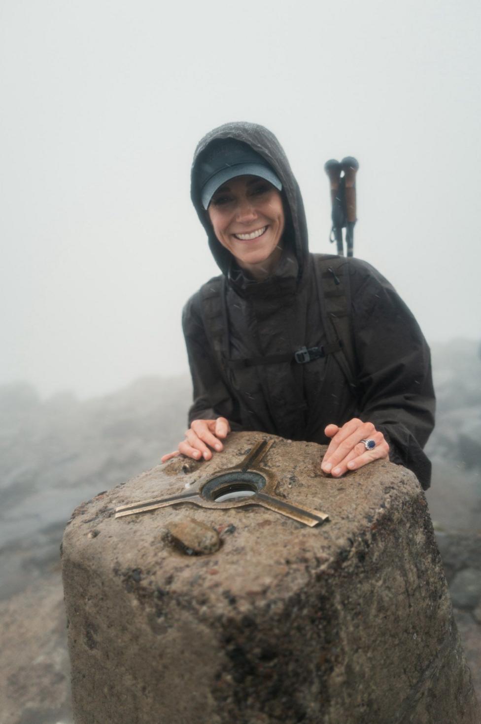 Catherine stands in a raincoat the summit of Ben Nevis