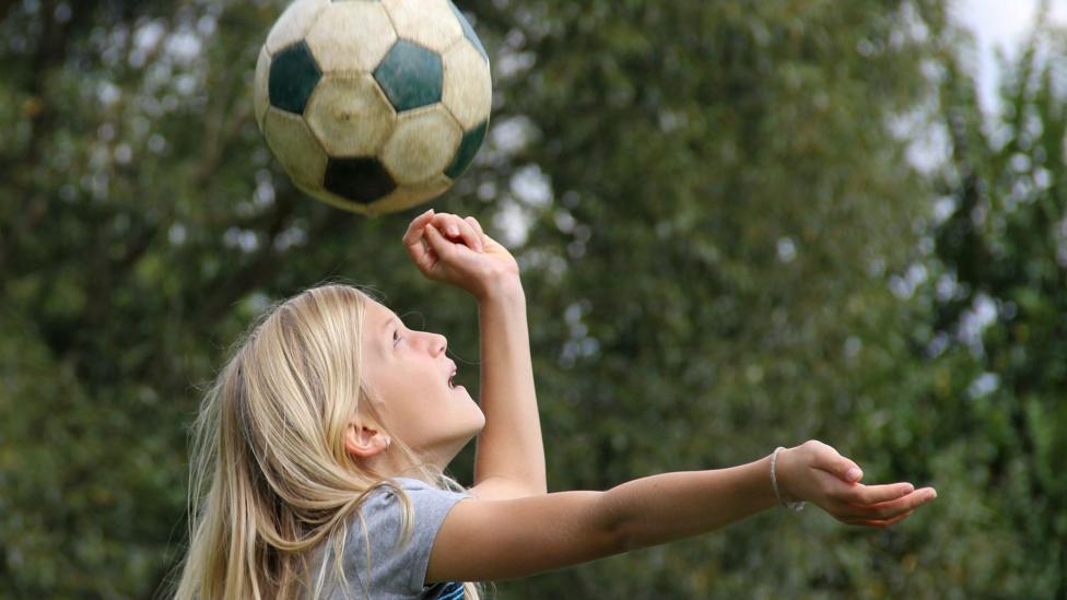 Girl heading a football in a park.