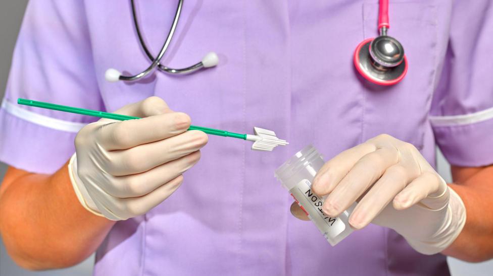 A nurse holds a plastic medical pot and a smear test brush