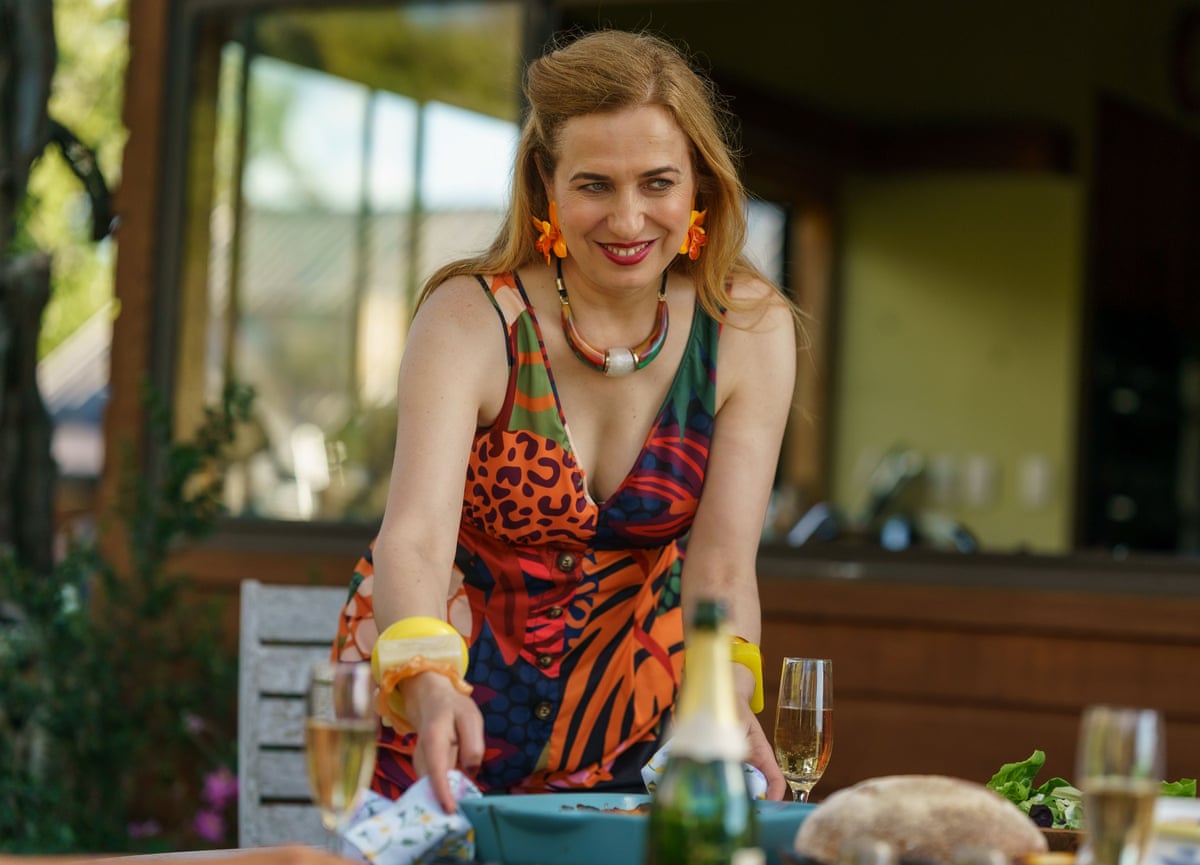 A woman wearing a bright dress at the dinner table in front of bottles of champagne