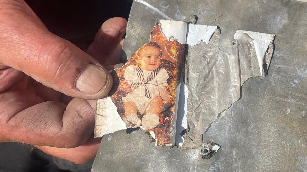 Close-up of Alan Needham's hands holding a slate with a torn photograph of a baby attached to the surface.