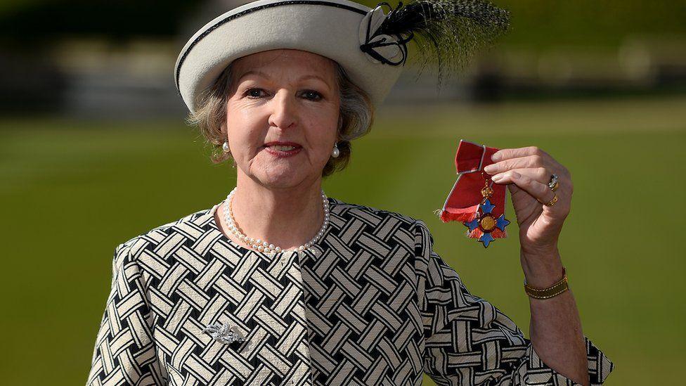 Penelope Keith being made a dame. She is dressed in black and white and holding up her medal for the cameras 