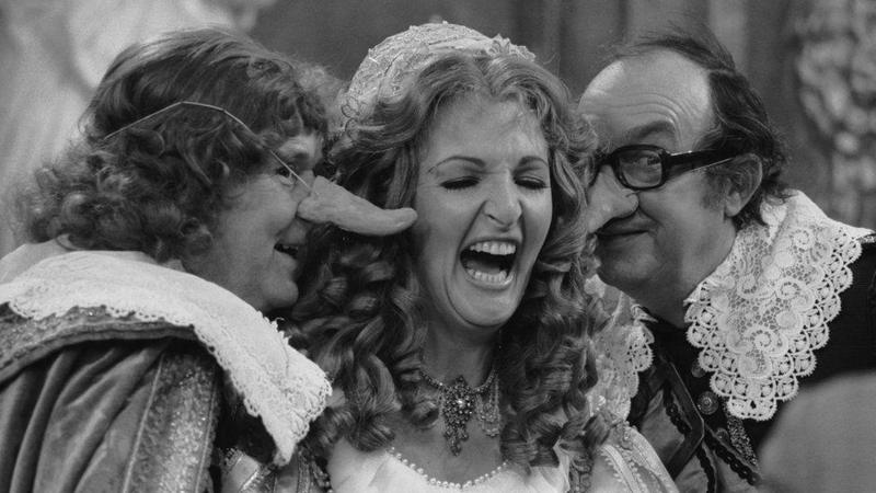 Penelope Keith on Morecambe and Wise. They are dressed as if they were members of the French court and the two men are wearing comedy noses. Keith is laughing.