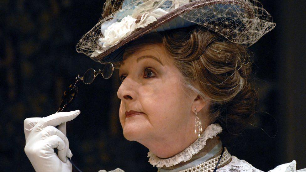 Penelope Keith as Lady Bracknell. She is looking fierce and peering through her glasses 