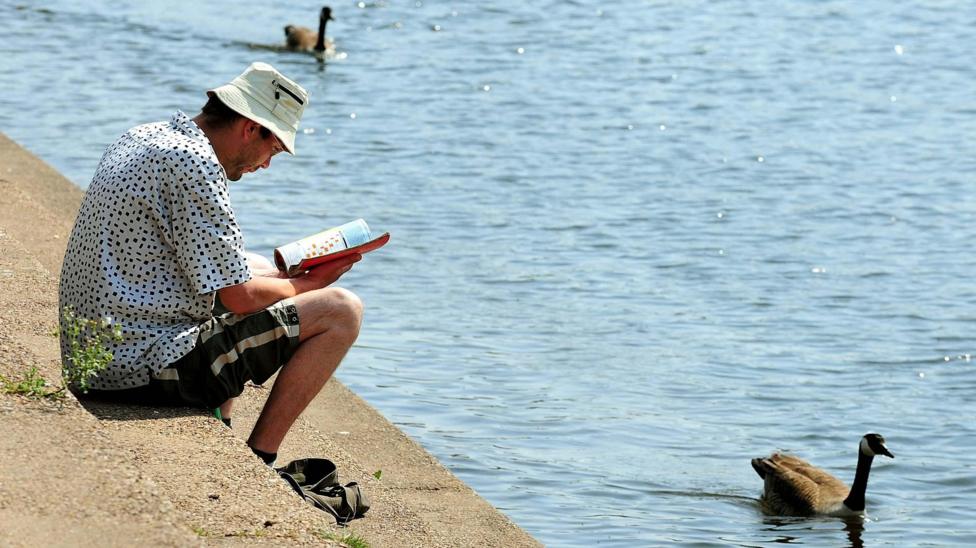 A man reading a book while geese swim past on the River Trent