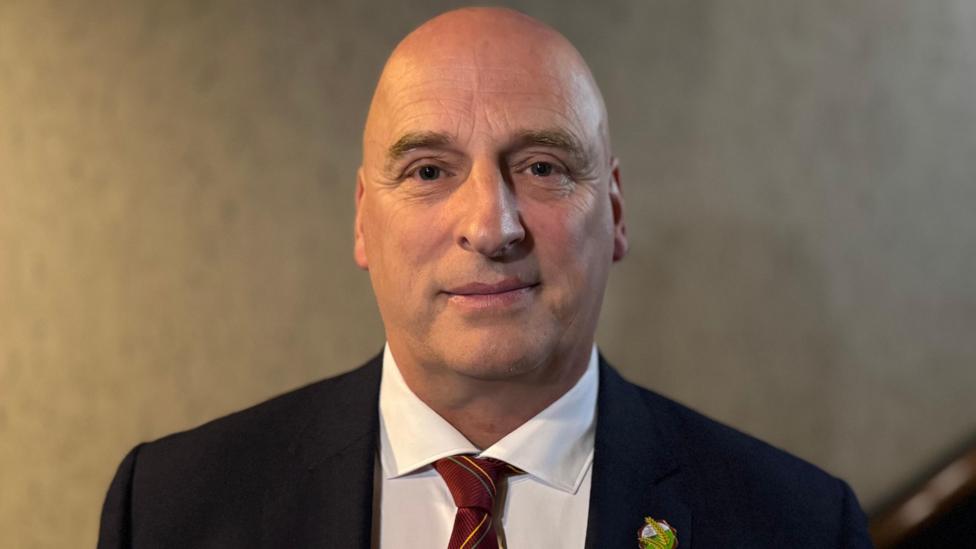 A man wearing a dark blazer and white shirt with red tie