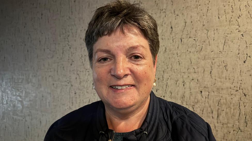 A woman with dark hair wearing a dark jacket and top