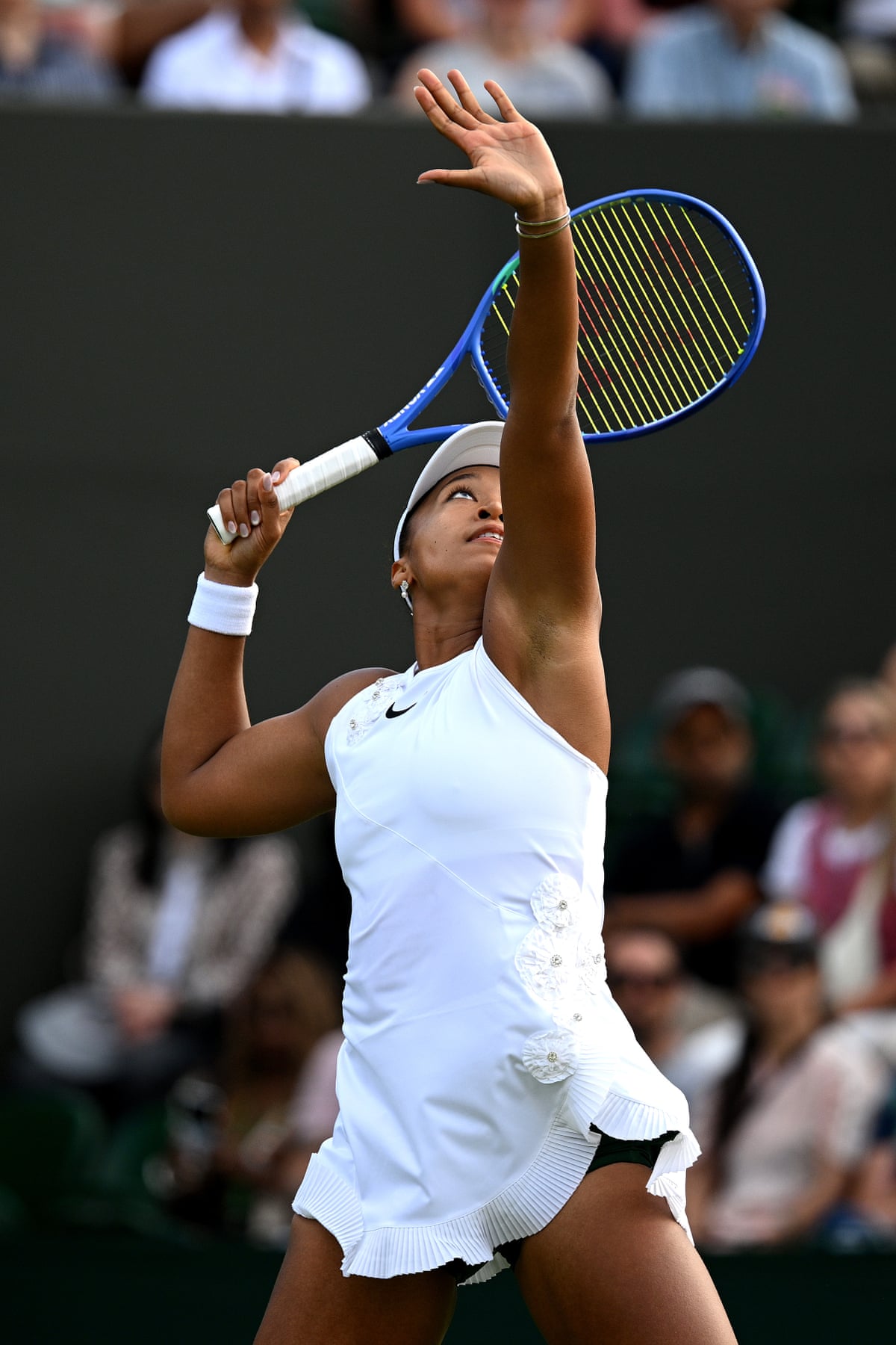 Naomi Osaka of Japan serves wearing a white Nike dress adorned with 3D flowers with bejewelled centres