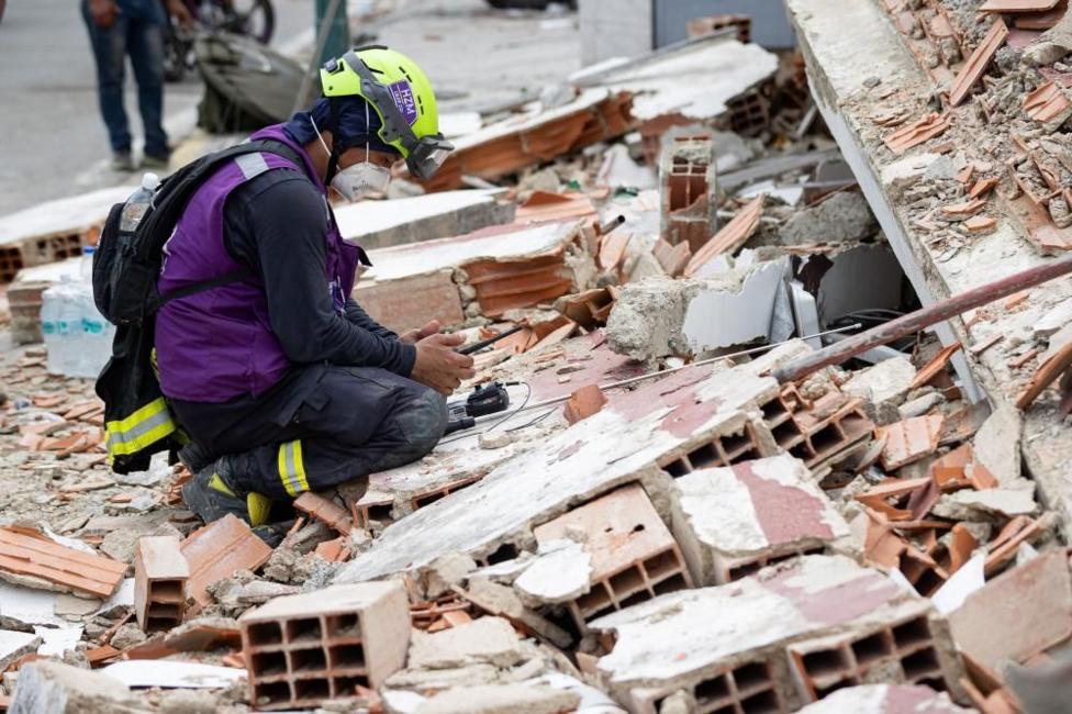 A rescue worker wearing a helmet, face mask and purple vest uses a sound detection device on the rubble of a building in Catia La Mar, Venezuela.