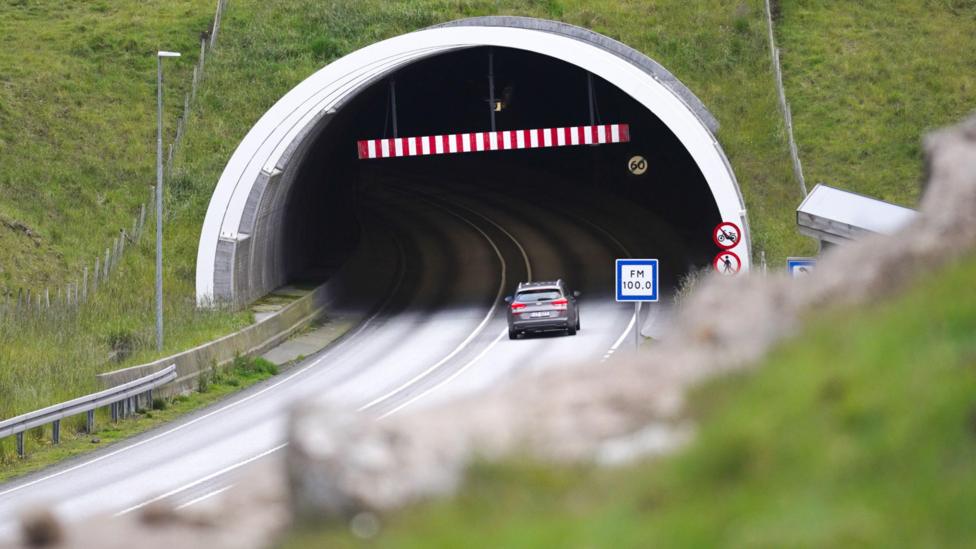 A grey car enters a tunnel, driving past red 