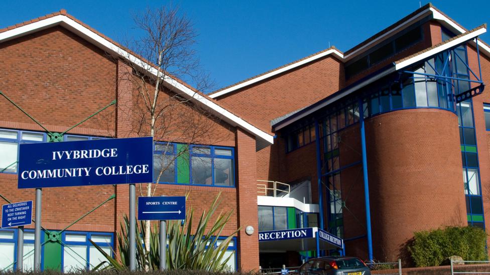 Ivybridge Community College, a red-brick post-modern building which appears to date from the 1980s or 1990s, with angular pitched roofs, curved brickwalls, blue window frames and green accents.