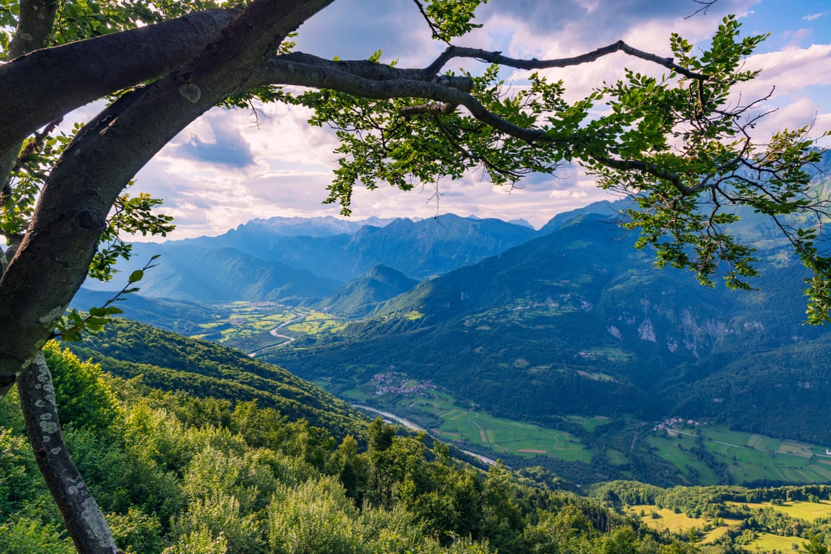 Pink sunset on a mountain top with a view of a green alpine valley with a river and mountains in the distance