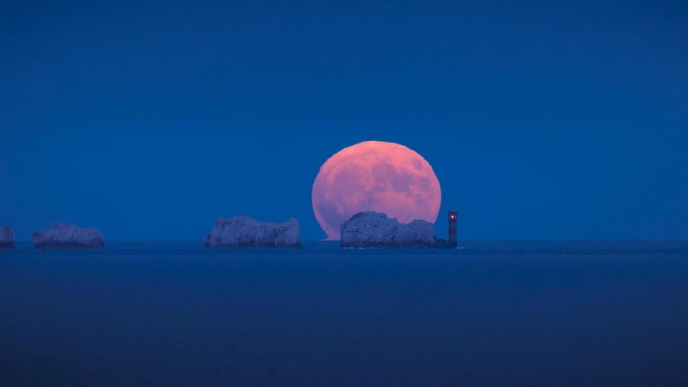The full strawberry moon rising above the Needles on the Isle of Wight taken from Highcliffe beach