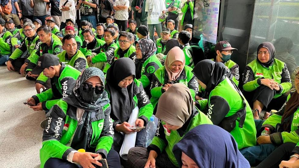 Gojek drivers wearing green uniforms seated outside a Jakarta courthouse where a verdict in the corruption case against the app's founder Nadiem Makarim is being delivered.