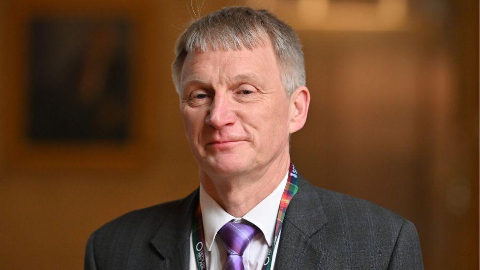 Ivan McKee, who has short grey hair, smiles at the camera. He is wearing a business suit