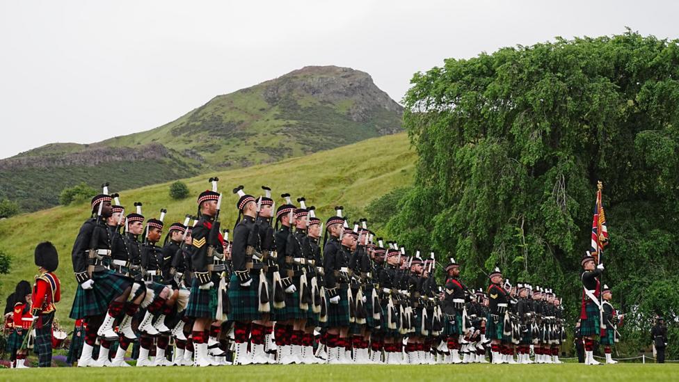 Lines of soldiers and military personnel wearing uniforms in the gardens on the Palace of Holyroodhouse. Arthur Seat is in the background.