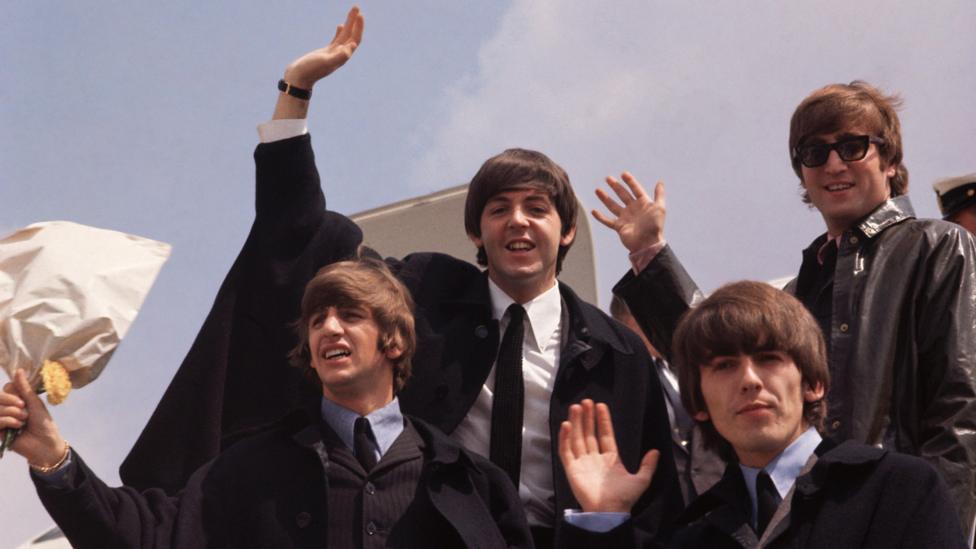 The Beatles wave as they step off an airplane in 1964