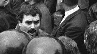 A black and white photograph of a Freddie Scappaticci in a crowd during an IRA funeral in the 1980s. He has black hair and a thick black moustache. 