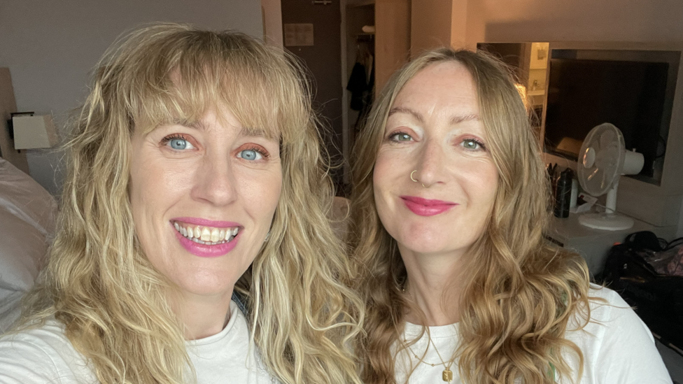 Nicola and Lowri. Both have long wavy hair and are wearing pink lipstick and white t-shirts. 