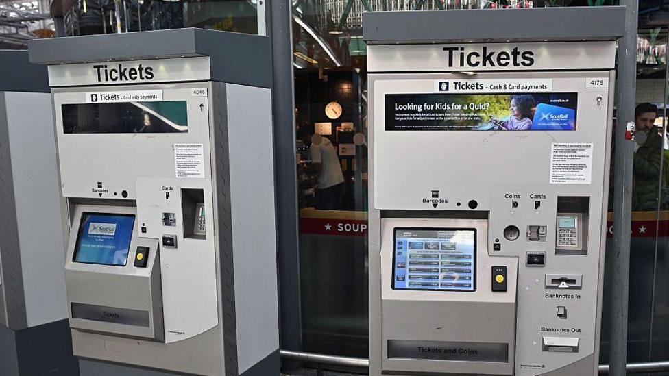 Two large grey ticket machines at a train station.
