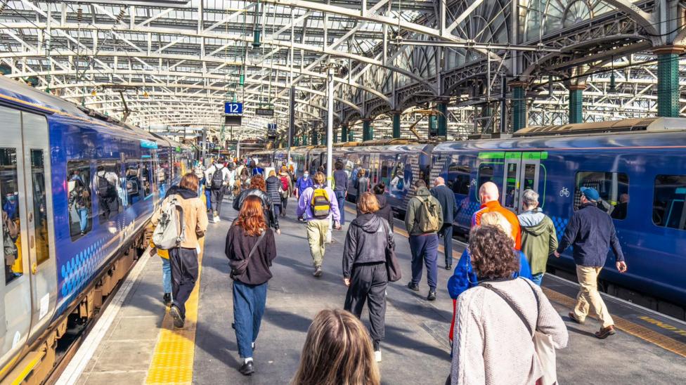 Two blue ScotRail trains on either side of a platform. Passengers are walking along the platform.