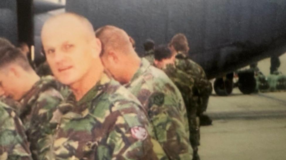 an old picture of a smiling soldier and other soldiers in camouflage uniform