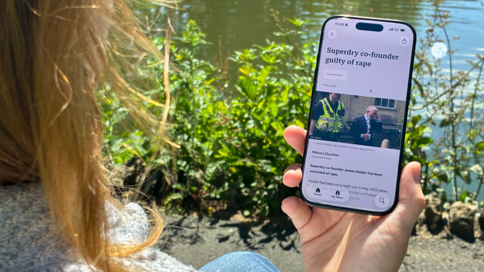 A woman looks at a story on a mobile phone. You can only see her hair and hand. The headline reads: Superdry co-founder guilty of rape.