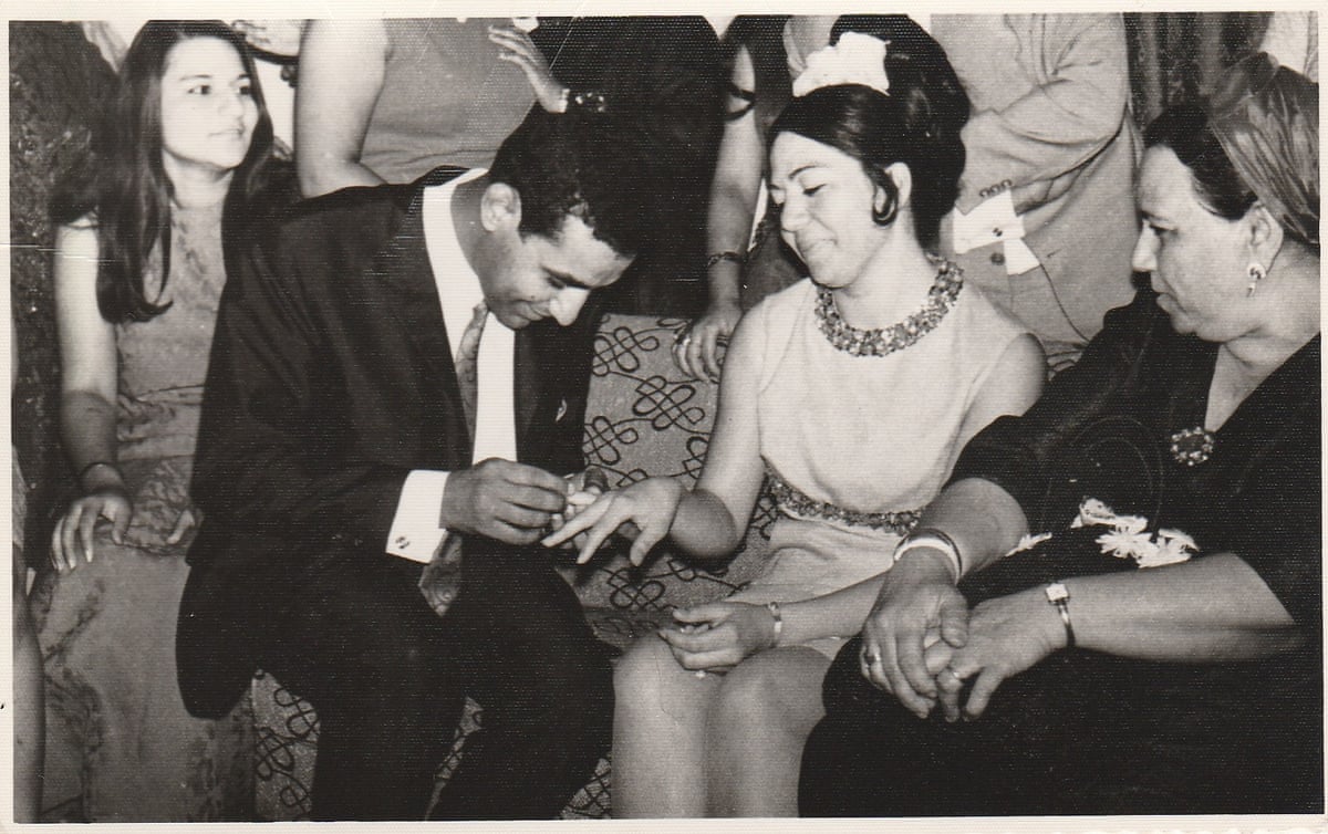 A man puts a ring on the finger of a smiling woman, while other people watch.