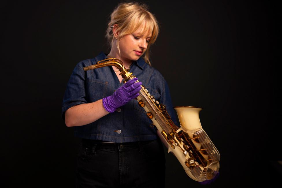 A woman with blonde hair holds a saxophone