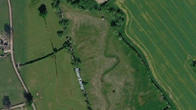 A satellite image showing the River Kemp from above, surrounded by bright green fields. On the right, you can see the indent of the river's natural meander etched into the field.