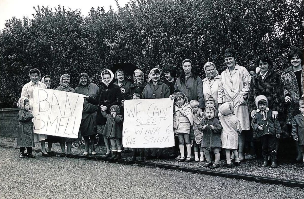 A black and white image of a group of women and children with banners reading: We can’t sleep a wink for the stink and Ban smell. 