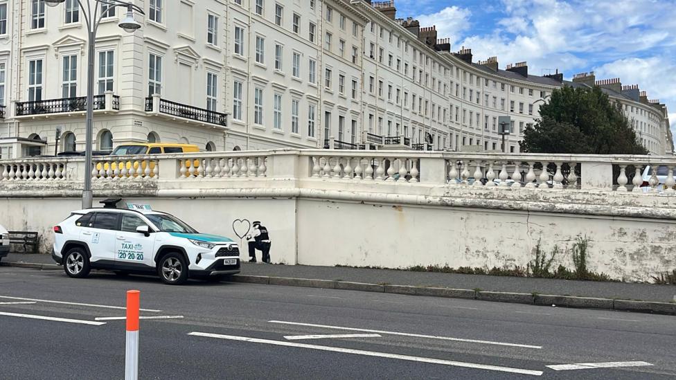 The mural on a wall with the regency buildings of Palmeira Square behind. A taxi is parked next to it