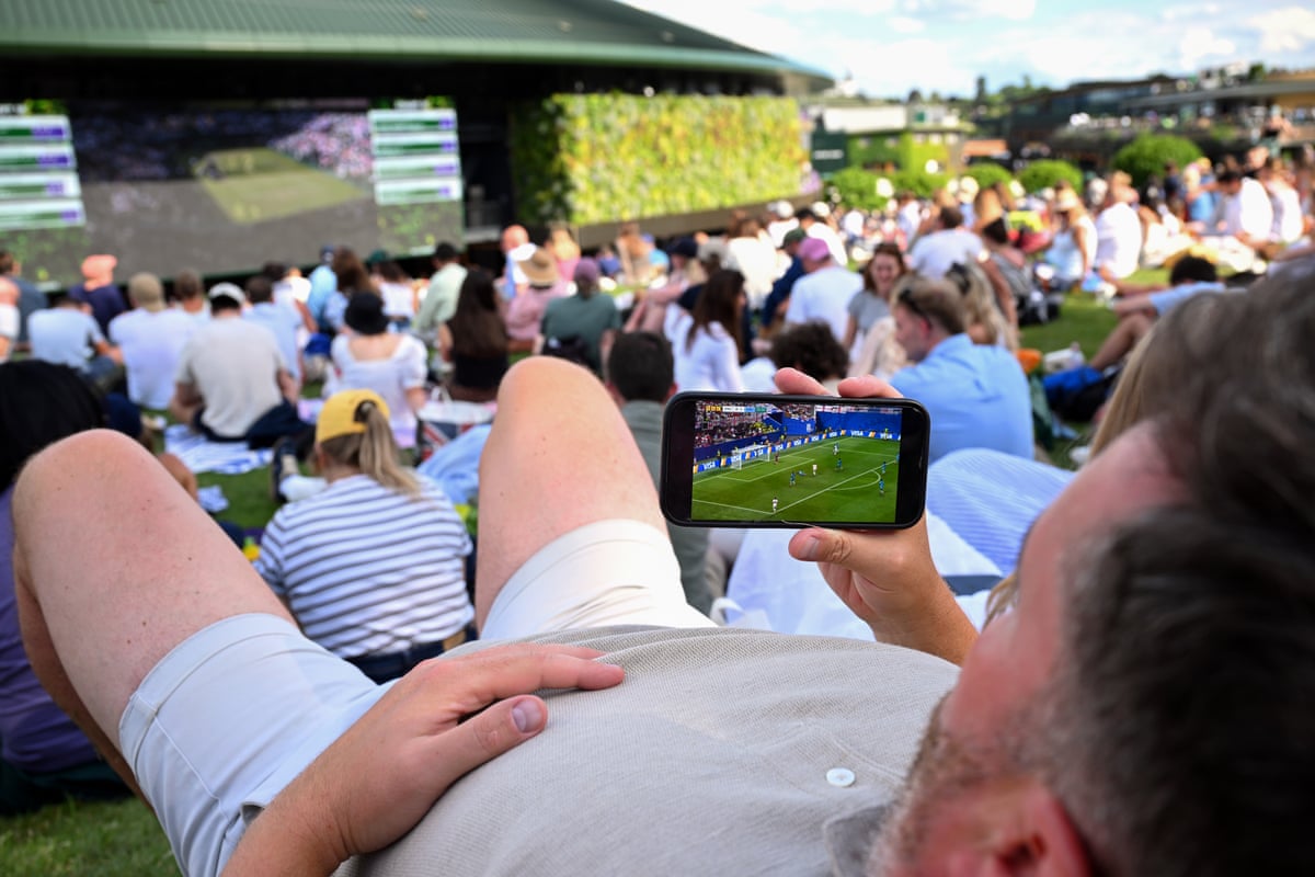 A fan on Henman Hill watches the football on his phone