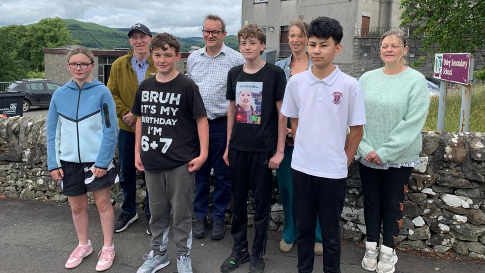 A group of four children and four adults stand in front of Dalry Secondary