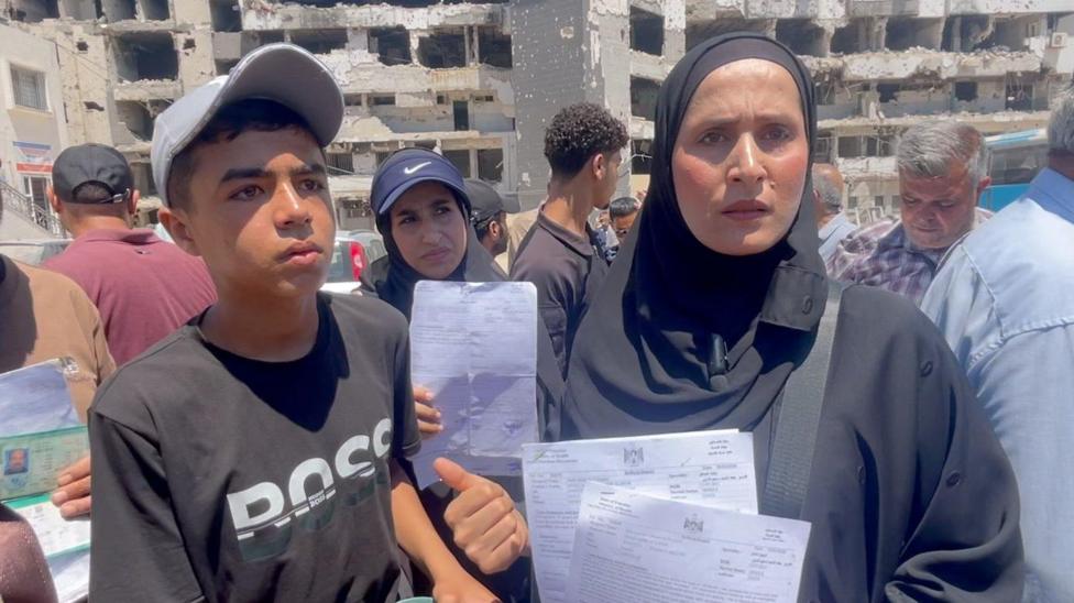 Umm Samir al-Dini (R) stands next to her son Muath, who is using crutches (L), outside al-Shifa hospital in Gaza City, northern Gaza