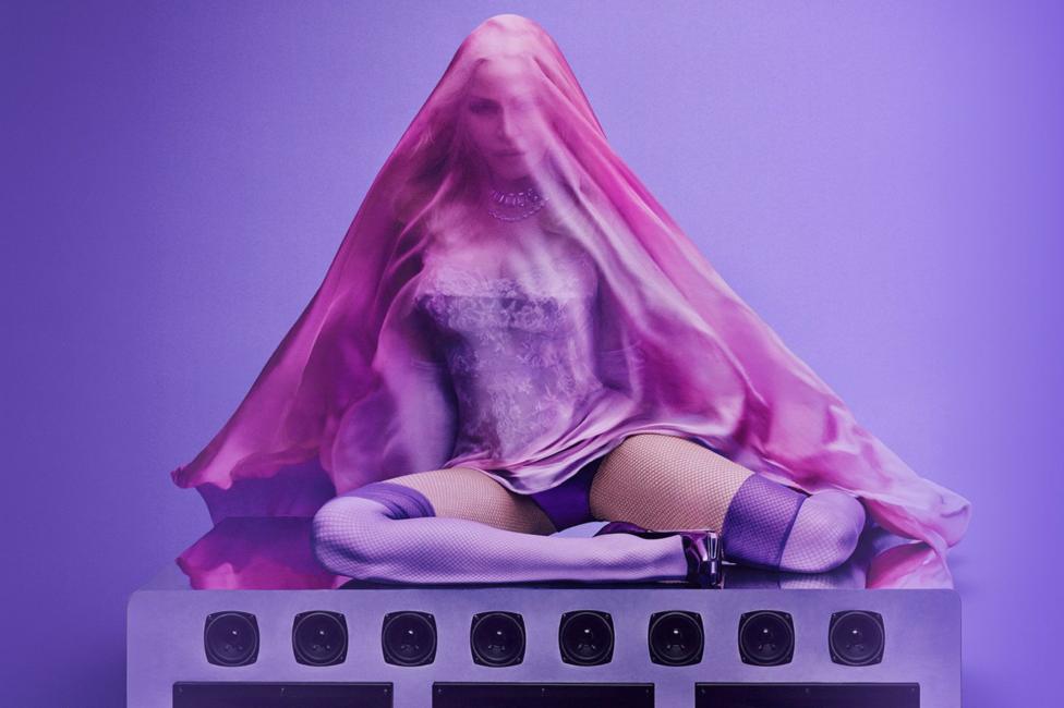 Madonna sits on top of an array of speakers, covered in a pink/purple veil, as part of the cover art for her fifteenth album, Confessions II.