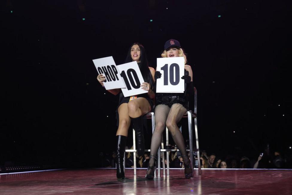 Madonna on stage with her daughter Lourdes in 2023. They are sitting on high stools, holding up score cards.