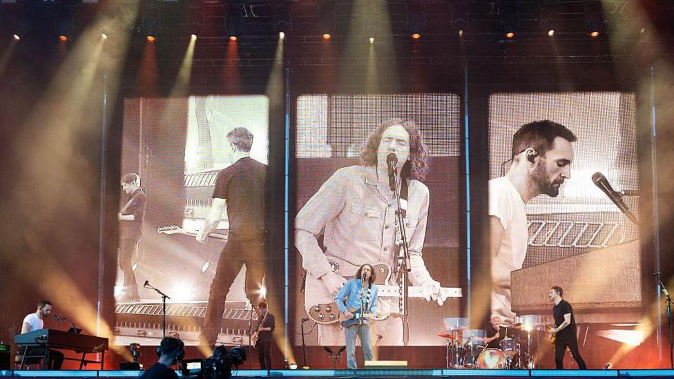 Snow patrol performing on a stage with a large screen behind them. 