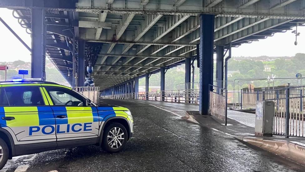 A police car is parked on the bottom deck of the craigavon bridge. the bridge is empty of traffic