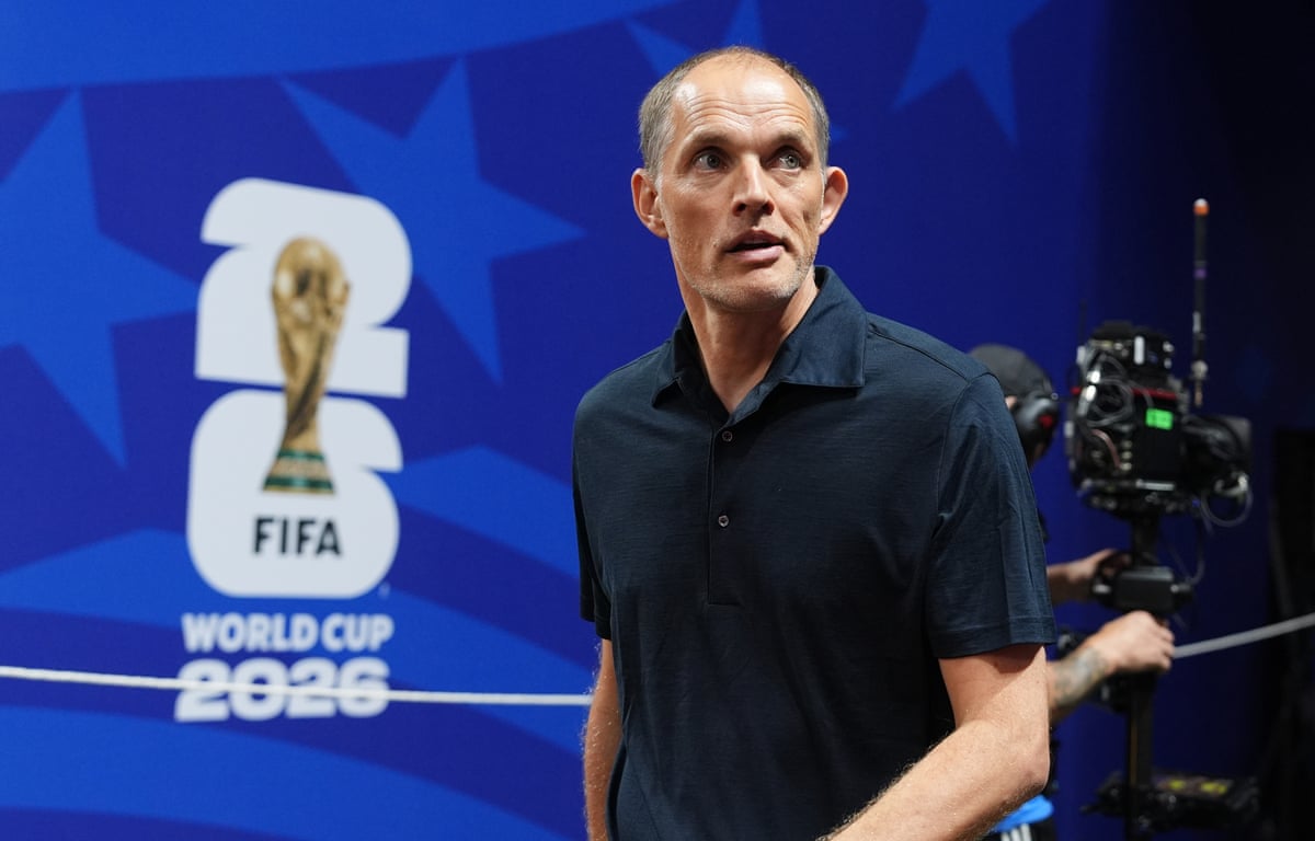 Thomas Tuchel standing at a press conference with a FIFA World Cup 2026 and a TV camera behind him