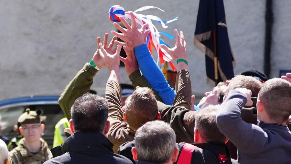 A group of men battle for a ball with ribbons attached