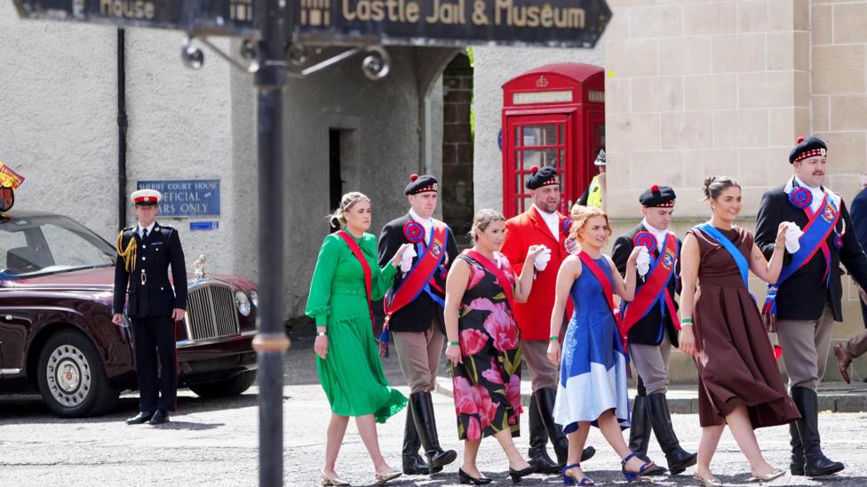 A group of men and women in colourful dress walk hand in hand through Jedburgh