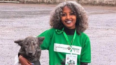 Feven Melese wears a green top and lanyard. She poses with her arm around a dog.