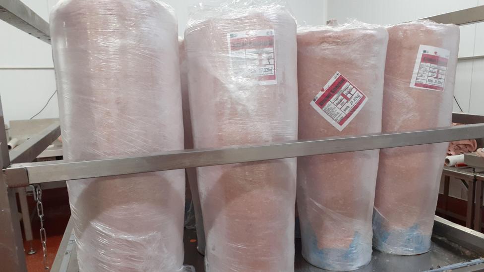 Four pink looking uncooked donor kebabs all wrapped in cling film standing on a trolley in a food processing factory